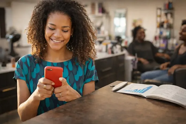 Succès d’une coiffeuse locks : de 800€ à 5000€ par mois grâce au digital Coiffeuse locks utilisant son smartphone dans un salon, illustrant la croissance de son chiffre d’affaires grâce à la digitalisation